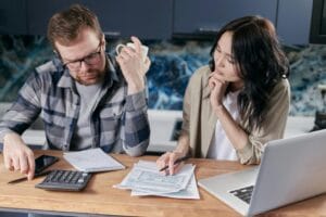A couple reviews taxes and documents on a laptop while discussing household finances.